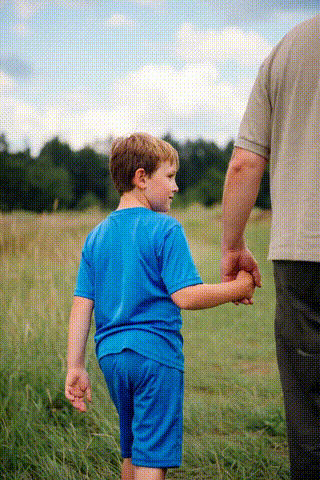 A child and an adult holding hands while walking through tall grass in an open field.